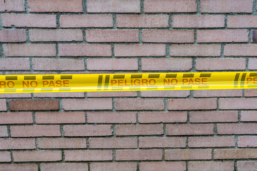 This image depicts a cordoned-off brick wall sealed with a prominent yellow band bearing the warning message in Spanish: 