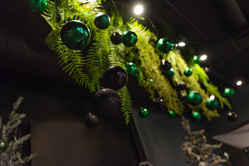 Elegant Christmas decorations featuring a mix of shiny green and black ornaments hanging amongst vibrant green ferns, creating a festive atmosphere.