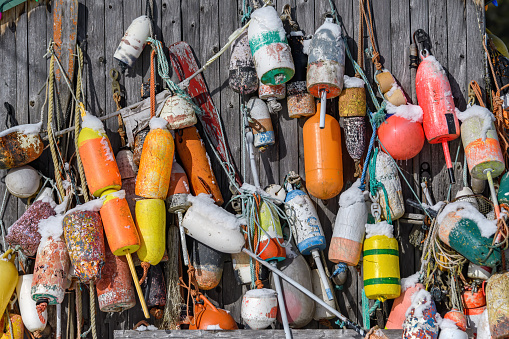 Many fishing buoys hanging from the side of a faded wooden building. These are the type of buoy used by commercial fishermen.