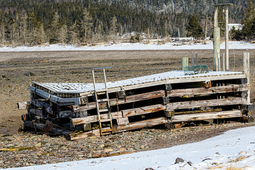 An old broken dock lying on a rocky beach in winter. The dock is covered with snow on the top but the beach is rocky.
