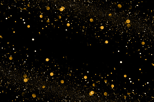 Gold bokeh and shinhing particles on black backound for magic design.