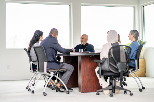 A small group of likeminded business professionals meet together to collaborate their ideas.  They are each dressed professionally and seated around a boardroom table.