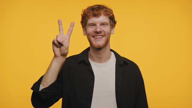 Smiling Man Giving Peace Sign Isolated on Yellow