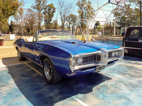 Lanus, Argentina - Sept 24, 2022: Old blue shiny sport 1969 Pontiac GTO two door convertible in a park. Front view. Nature, trees. Classic luxury muscle racing car.