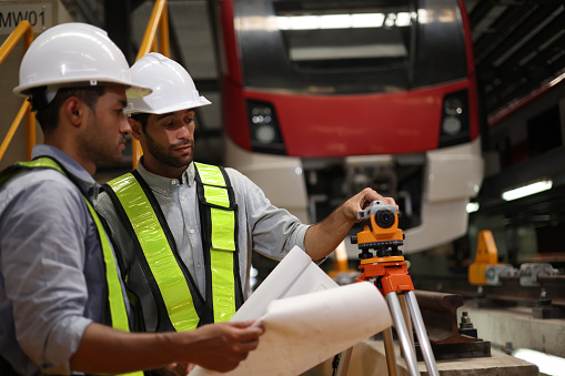 Two skilled electric train engineers are diligently surveying and checking to ensure the plan matches the blueprint and survey camera in the electric train maintenance shop, to submit work on the specified date.
