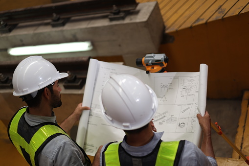 Two skilled electric train engineers are diligently surveying and checking to ensure the plan matches the blueprint and survey camera in the electric train maintenance shop, to submit work on the specified date.