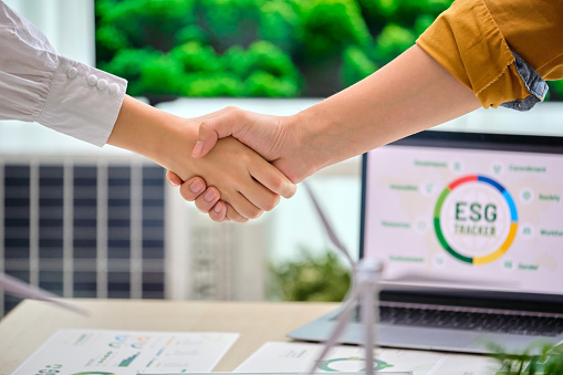 Close up business hand    shaking hands when successful deal agreement ,having a ESG meeting environment, society and governance, discussing renewable energy with wind turbine  and solar panel at office,Save the planet go green eco-friendly  net zero emission clean business  ethical