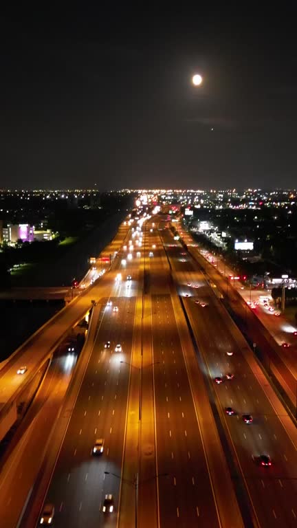 Drone footage of the vehicles driving on the highway roads and the illuminated cityscape at night