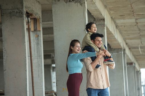Excited young father carrying son while discussing new house plans with woman at construction site