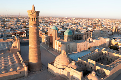 Bukhara Poi Kalan Complex and Kalan Minaret. Warm Sunset Light over the famous Kalyan Poi Kalon Minaret, Poi Kalan or Po-i-Kalyan and Mir Arab Madrasah in the center of the old town of Bukhara - Buxoro - Бухорo. Aerial Drone Point view in warm sunset light. Itchan Kala, Bukhara, Khorezm Region, Uzbekistan, Central Asia.