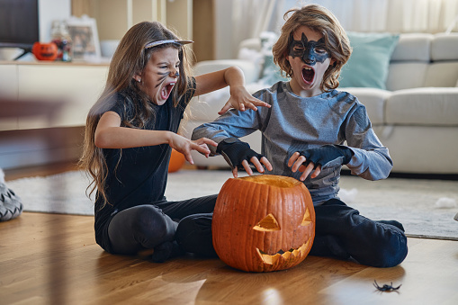 Children playing hocus pocus on a Halloween day. They are indoors with a pumpkins, playing around, dressed up in costumes.