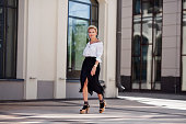 Confidence and sophistication mature woman walks city streets in fashionable ensemble chic white shirt and black fringed skirt with high heeled sandals and socks, fashion icon of style