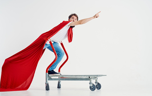 a superhero in a red cloak stands on a cargo cart In a bright room. High quality photo