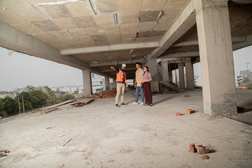 Male architect explaining progress of house building to young couple while working at construction site