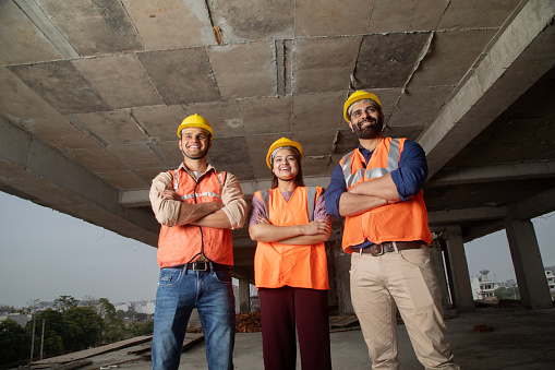 Low angle view of confident architects in protective workwear with arms crossed smiling and standing inside building at site
