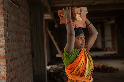 Mid adult female worker carrying bricks on head while working in building at construction site