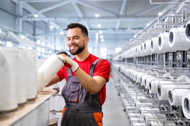 istock Textile factory worker with thread spools and industrial sewing machine in background. 2126823428