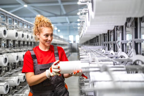 istock Female textile factory worker holding thread spool and working on industrial knitting machine. 2126823433