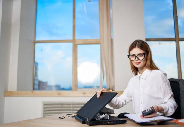 Beautiful mid adult businesswoman financial advisor working at her desk in the office, looking at monitor and reading investment project review