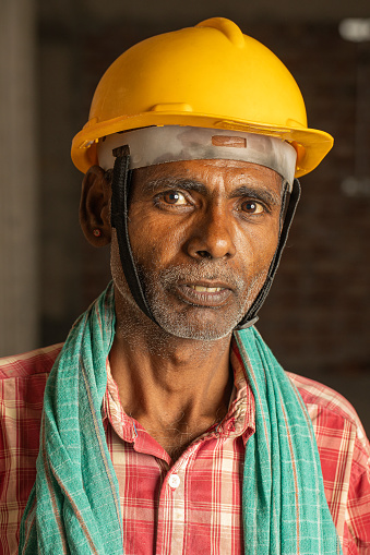 Portrait of senior male mason standing by brick wall at construction site