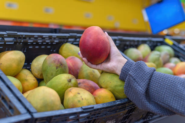 istock Hand holding a mango at a supermarket. 2126858049