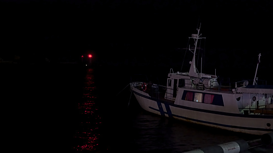 Fishing boat at the pier at night. There is a lighthouse in the background