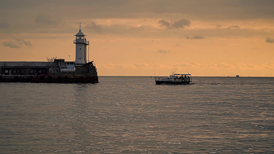 Fishing motorboat and lighthouse against the sky at dawn.