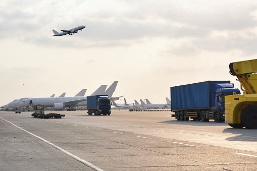 A busy airport scene with a truck passing by, cargo planes lined up, and a plane ascending into the sky, capturing the constant movement of air freight operations.