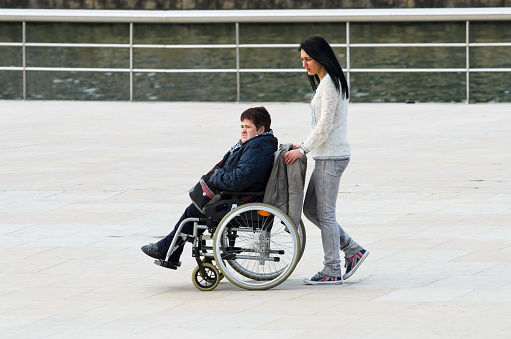 Bilbao, Spain - april 4, 2014: A woman in a wheelchair is helped by another woman strolling in the streets of the city of Bilbao.