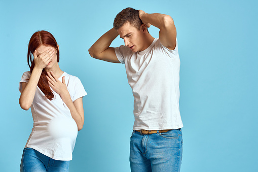 Pregnant woman in white t-shirt and man married couple waiting for baby blue background cropped view of emotions. High quality photo