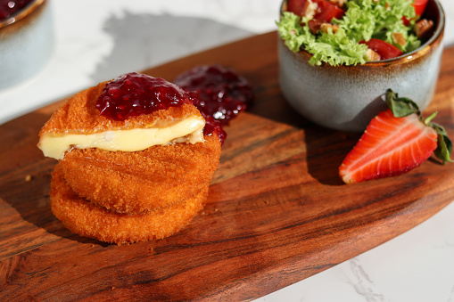 Fresh made fried camembert cheese with cranberry sauce on top, grey stone plate and blurry white background