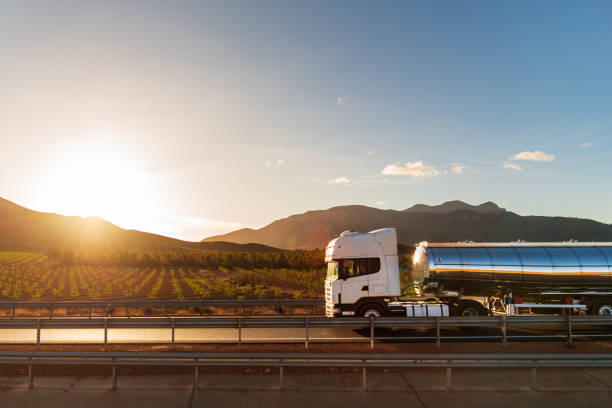 Truck with a food tanker driving next to a field of vineyards with the sun rising between the mountains, side view. Truck with a food tanker driving next to a field of vineyards with the sun rising between the mountains. wine shipping stock pictures, royalty-free photos & images