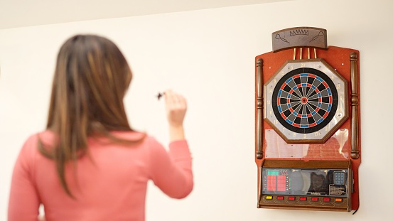 Rear view of a young caucasian woman playing darts at home