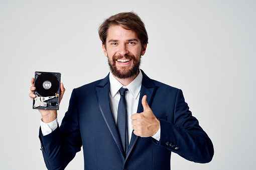 a man in a suit holds an unassembled hard drive in his hand and a gray background. High quality photo