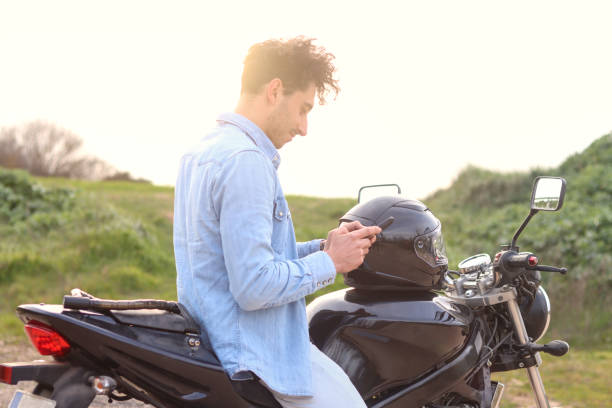 istock Curly haired Caucasian young man sitting on his motorcycle using mobile 2127175713