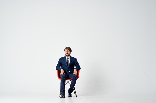 an elegant gentleman in a suit sits on a red chair in the middle of the room. High quality photo