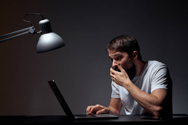 istock man with laptop sitting at table dark background workplace office emotions lamp gesturing with hands model cropped view 2127210454
