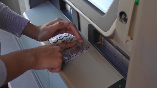 Woman's hands covering the PIN numbers she is pressing on an ATM