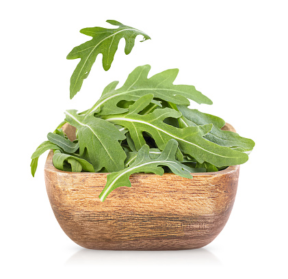 arugula in a wooden plate on an isolated white background