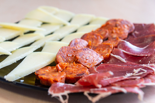 Iberian Delights: Cheese, Chorizo, and Ham on a Black Plate.