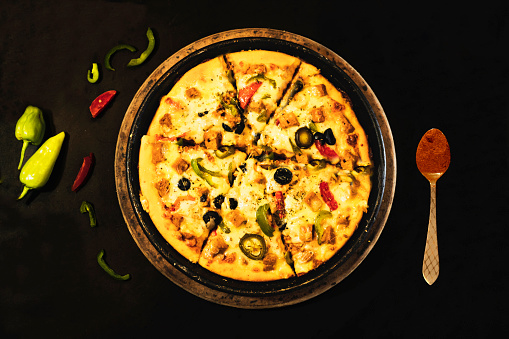 pizza in pan on a black background along with chillis