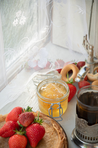 Still life in the Russian tradition for Maslenitsa, pancakes with honey and strawberries, tea in a faceted glass with a silver glass holder with bagels, Slavic holiday, high quality photo