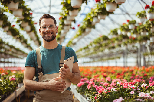 Portrait of happy gardener in greenhouse looking at camera while working in a plant nursery. Lifestyle, gardening, profession and people concept