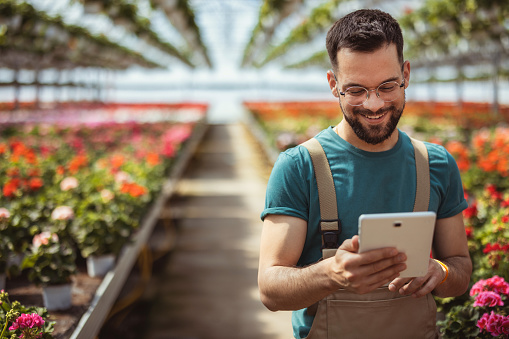 Portrait of a florist using digital tablet while working in a plant nursery. Gardening, technology and people concept.
