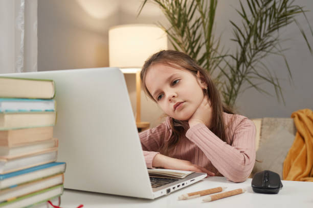 istock Online learning resources for children. Digital education platforms for kids. Tired sad little girl using laptop while sitting at table at home suffering neck pain 2127475147