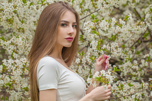 Nice fashion model with long brown hair and natural makeup against floral background outdoor