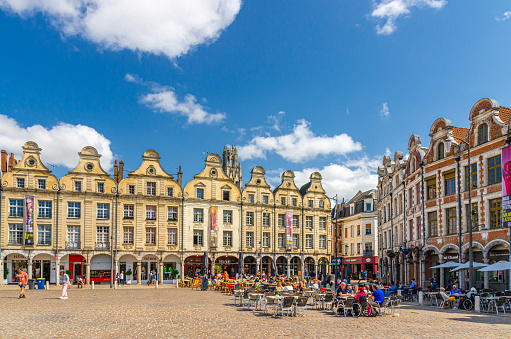 Arras, France, July 3, 2023: Flemish-Baroque-style townhouses buildings and street restaurant on Place des Heros Heroes Square in city center, blue sky in summer day, Artois, Hauts-de-France Region