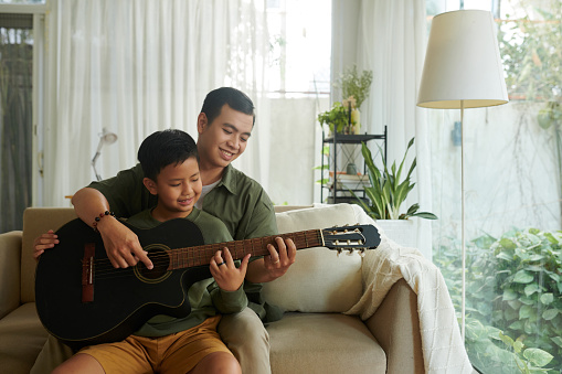 Happy father showing son how to hold guitar when playing