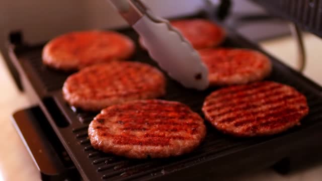 a woman fries hamburger patties on an electric grill. There is a grill in the kitchen. High quality FullHD footage