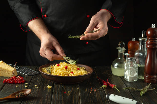 The cook adds rosemary to the pasta bowl for flavor and aroma. Work environment in tavern kitchen with spices and kitchen utensils